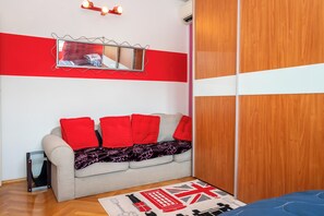 A room with a sofa, a mirror, a wooden wardrobe, and a red and white wall. - Apartment Near City Center (Split)