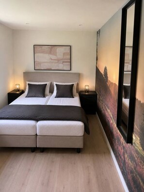 Una cama doble con cabecera, dos mesitas de noche con lámparas, un cuadro abstracto grande sobre la cama y un espejo grande en la pared.