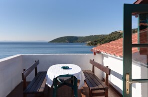 Een balkon met een tafel en banken, uitkijkend op een waterpartij en heuvels.