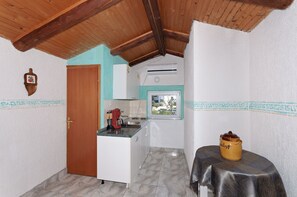 A compact kitchen with a wooden ceiling, a small table with a pot, and a window with a view. - Apartments and Room Gulic (Rab)