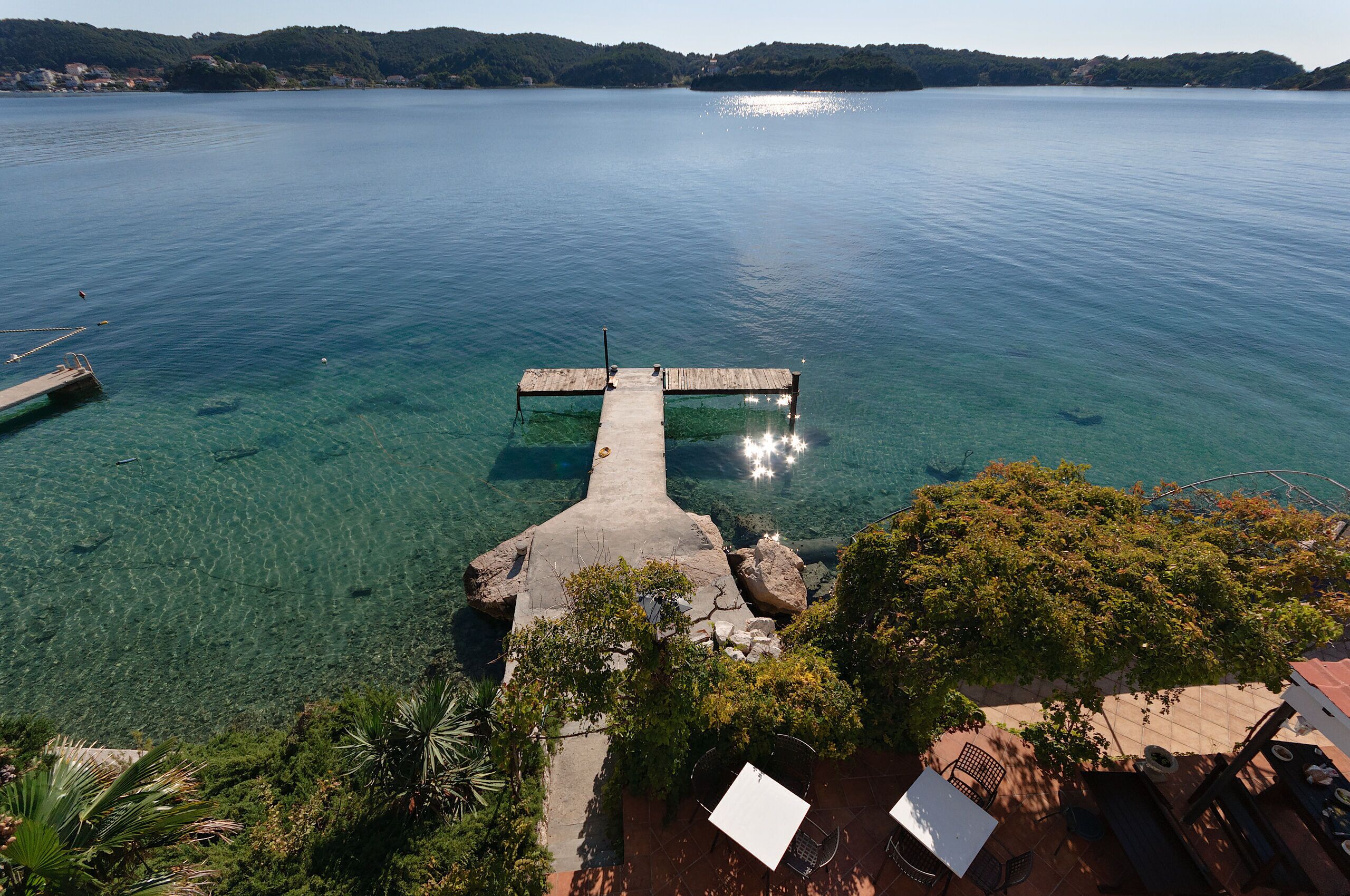 A clear lake with a wooden pier extending into the water, surrounded by greenery and a distant shoreline.
