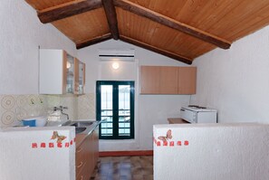 A compact kitchen with a wooden ceiling, a sink, cabinets, and a window with a view. - Apartments and Room Gulic (Rab)