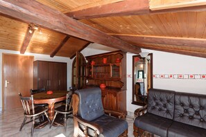 Een zithoek met een houten tafel en stoelen, een bank, een houten kast met rode objecten, en een spiegel aan de muur.