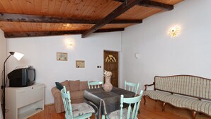 Um quarto aconchegante com teto de madeira, uma televisão sobre um móvel, um sofá, uma mesa de jantar com cadeiras e luminárias fixadas na parede.