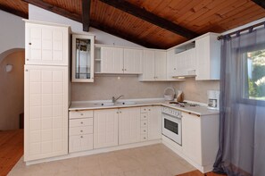 A kitchen with white cabinetry, a sink, a stove, and a window with a curtain. - Apartments and Room Gulic (Rab)