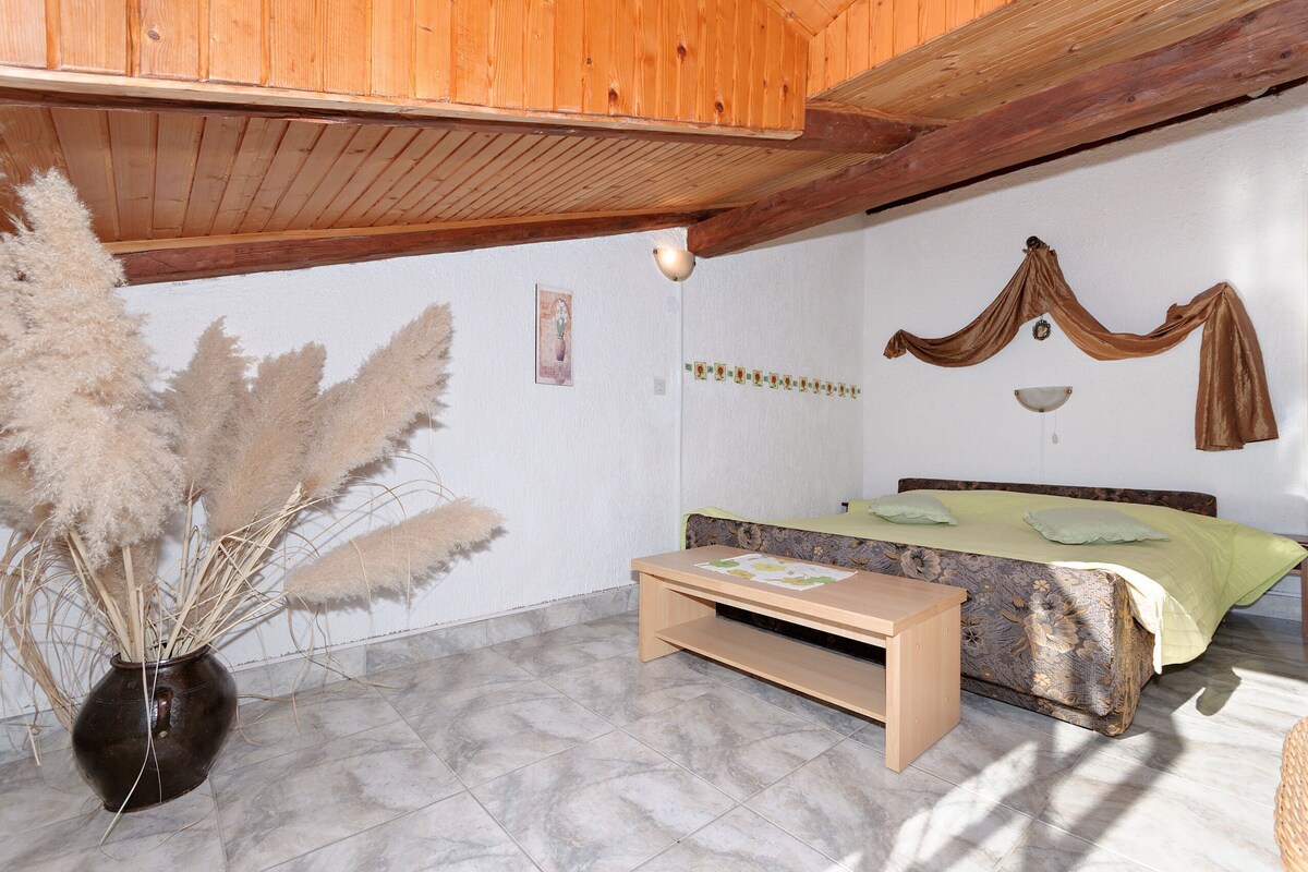 A bedroom with a bed, a bedside table, a hanging plant, and a wooden ceiling.