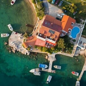 An aerial view of a coastal property with a house, a swimming pool, and several boats docked at a pier. - Apartments and Room Gulic (Rab)