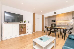 A modern living room with a flat-screen TV, a dining area with a table and chairs, and a kitchen with wooden cabinets and appliances. - Apartment Mariolina (Baska Voda)