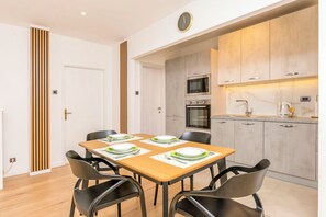 A modern kitchen with a microwave, oven, and cabinets. There is a dining table with chairs and a clock on the wall. - Apartment Mariolina (Baska Voda)