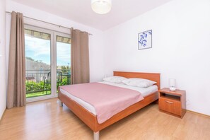 A bedroom with a bed, a nightstand, a window with curtains, and a small picture on the wall. - Apartment Mariolina (Baska Voda)