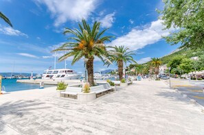A marina with boats, palm trees, and a paved walkway. - Apartment Mariolina (Baska Voda)