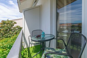 A balcony with a glass door, a small round table, two chairs, and a pair of sunglasses on the table. - Apartment Mariolina (Baska Voda)