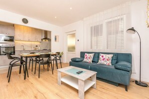 A modern living room with a sofa, coffee table, dining table, chairs, and a kitchen area with appliances. - Apartment Mariolina (Baska Voda)