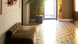 En hall med ett mönstrat golv, en bänk, en krukväxt och en dörr som leder till ett ljust område.