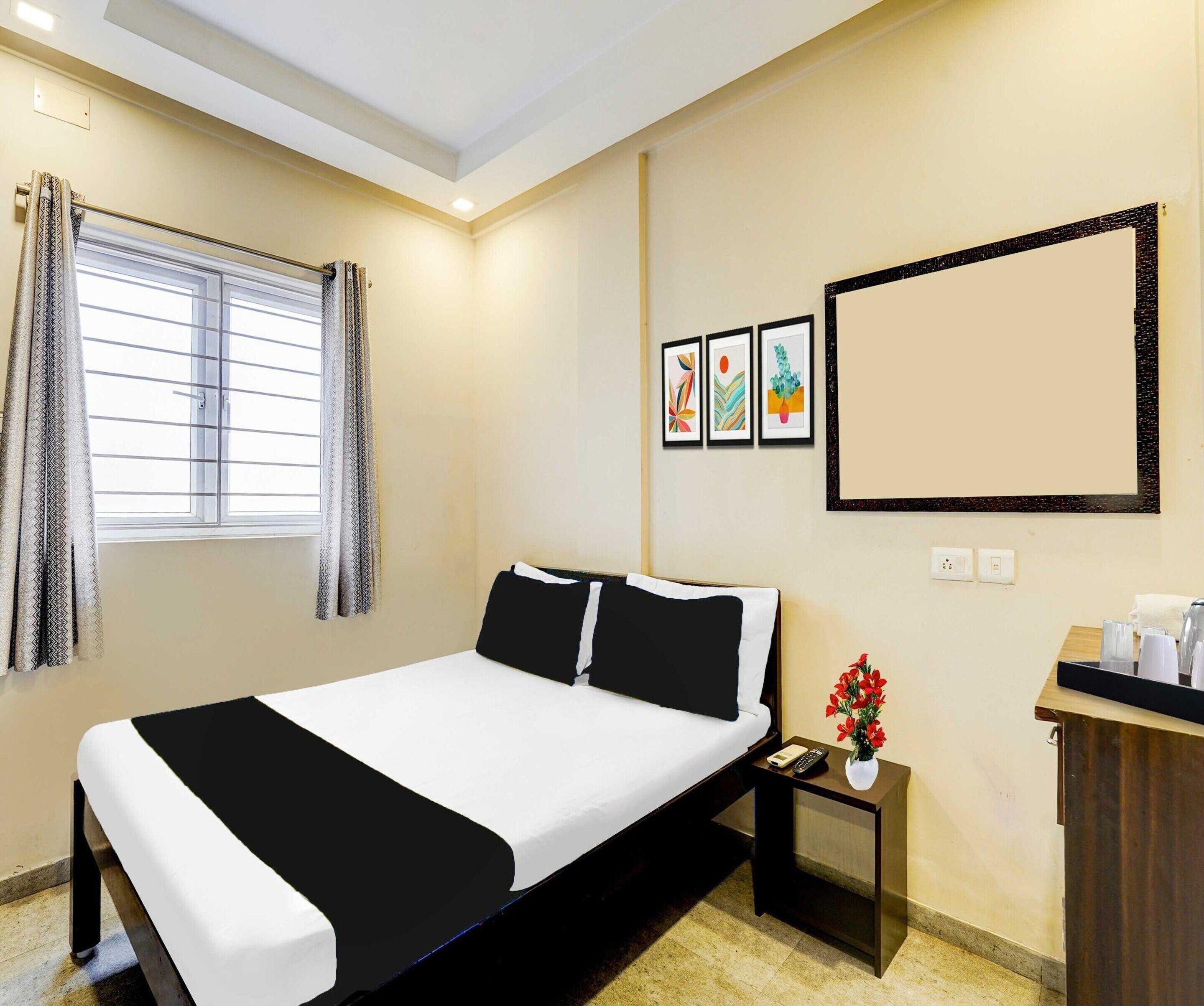 Quarto de hotel com cama, mesa de cabeceira, escrivaninha com um vaso de flores e janela com cortinas.