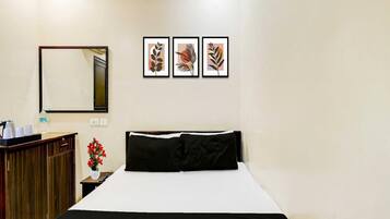 A hotel room with a bed, a nightstand, a mirror, and three framed artworks on the wall.