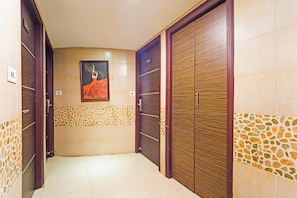 A hallway with two wooden doors, a tiled wall with a mosaic pattern, and a framed picture on the wall.