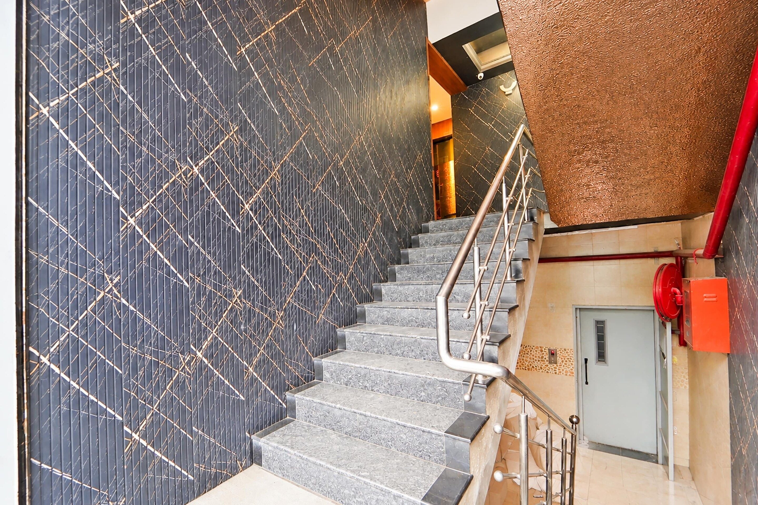 A staircase with a patterned wall and a red emergency pull station.