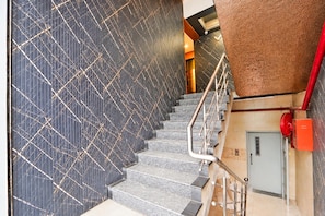 A staircase with a patterned wall and a red emergency pull station.
