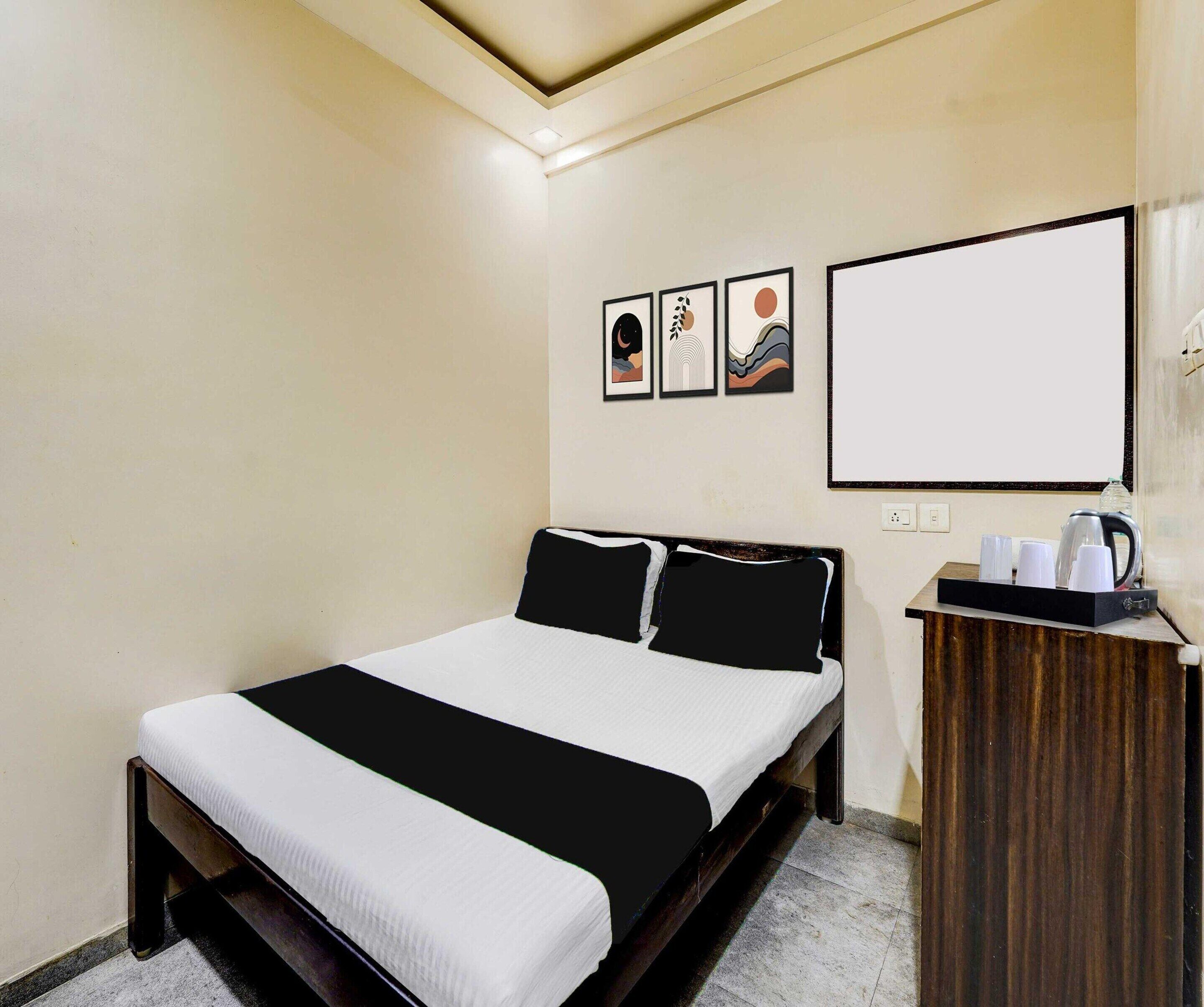 Quarto de hotel com cama, mesa de cabeceira com chaleira e três obras de arte emolduradas na parede.