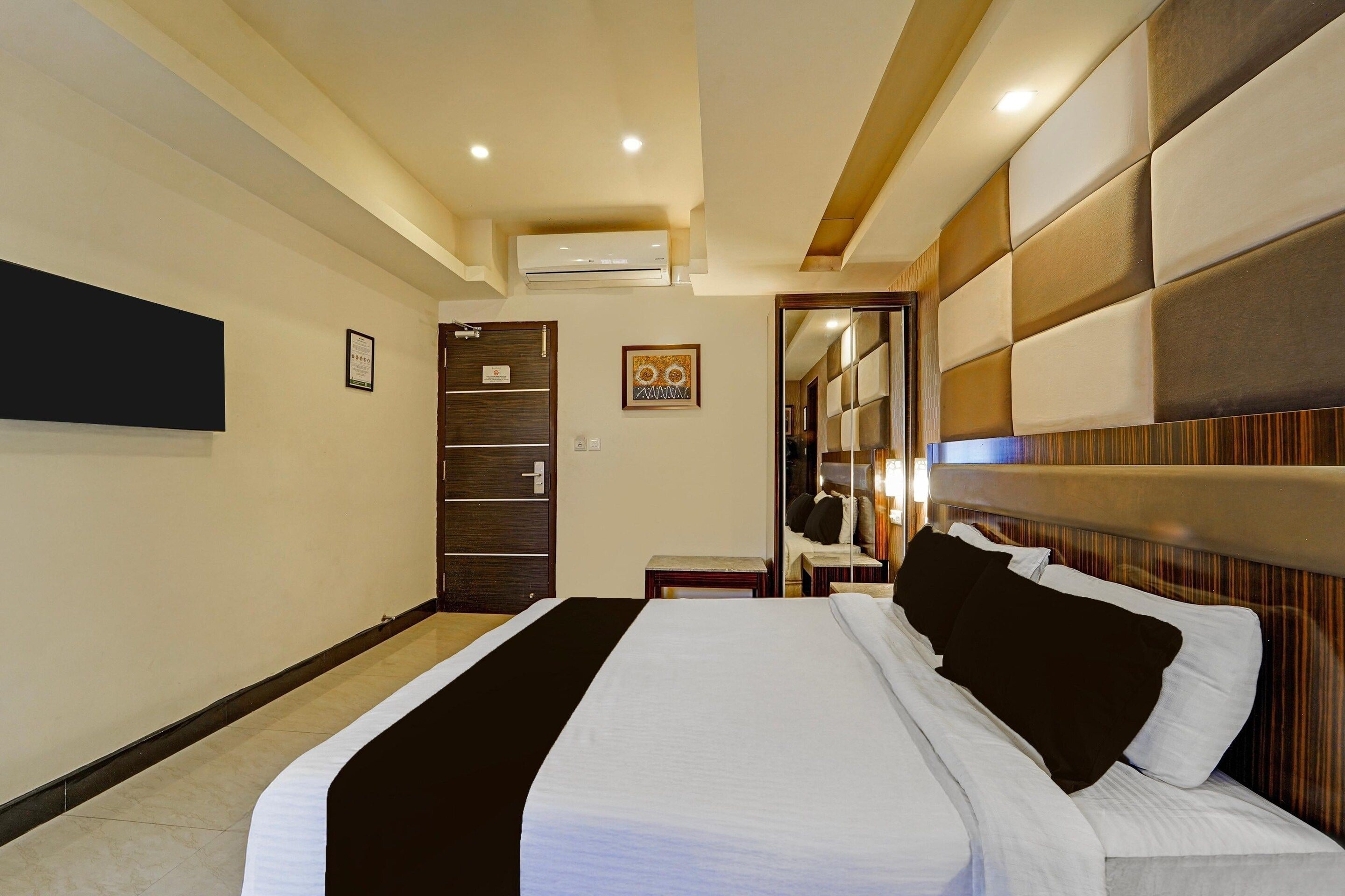 A hotel room with a bed, a desk, an air conditioning unit, a mirror, and a door.