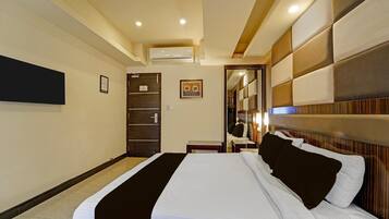 A hotel room with a bed, a desk, an air conditioning unit, a mirror, and a door.