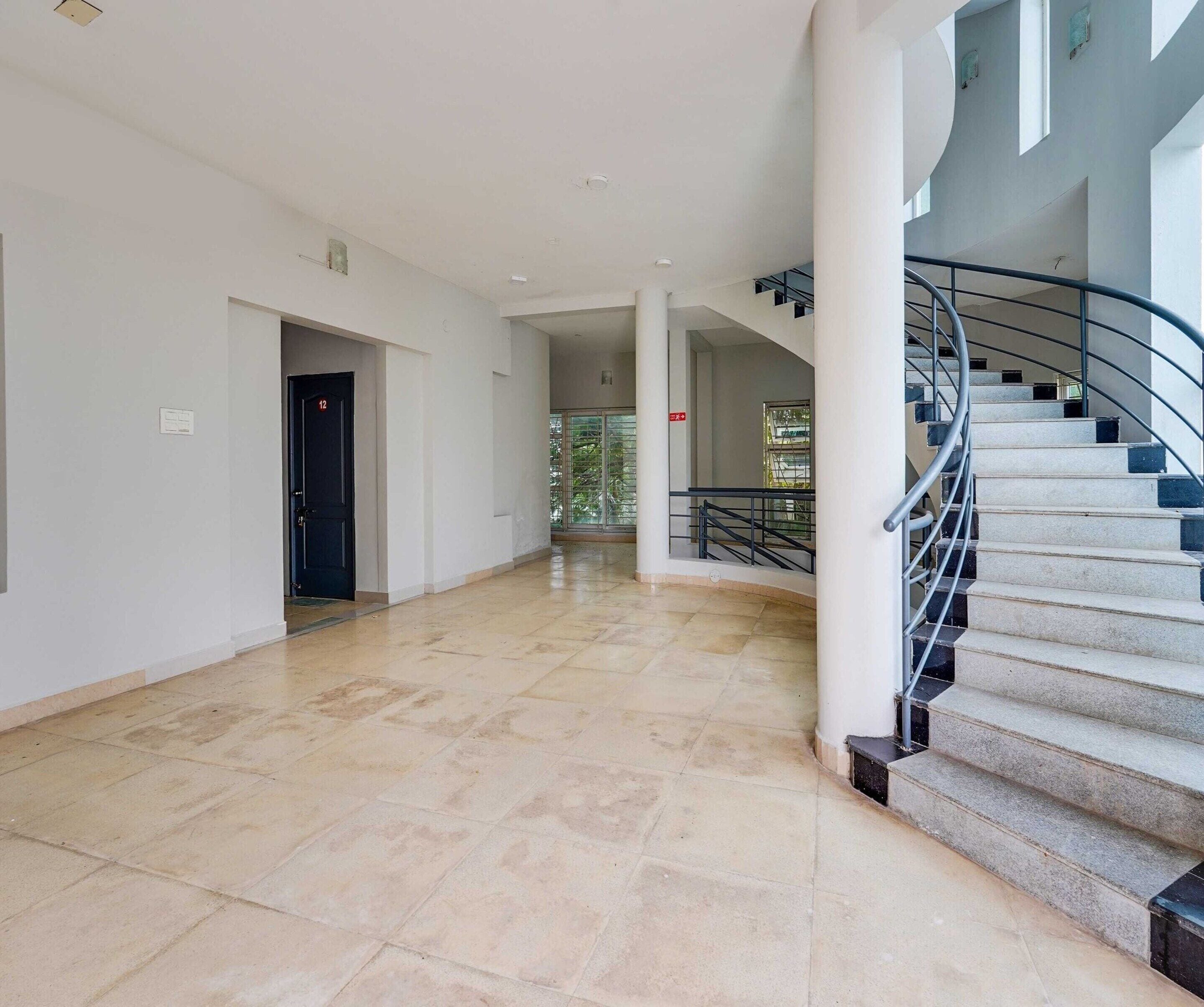 Um corredor amplo com piso de mármore, uma escada com corrimão de metal e uma porta com o número 12.