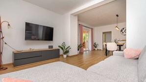 A modern living room with a grey sofa, a flat-screen TV, a wooden cabinet, and a dining area with a table and chairs. - House Melani (Zminj)