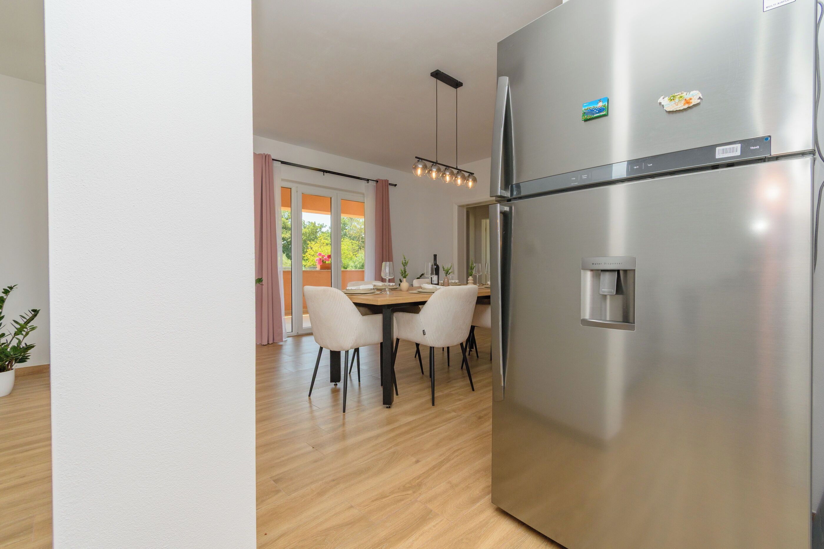 A modern kitchen with a stainless steel refrigerator, wooden dining table, and chairs.