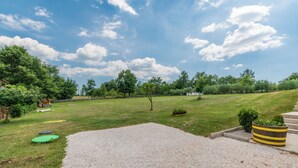 A grassy outdoor area with a gravel path, trees, and a small garden bed. - House Melani (Zminj)