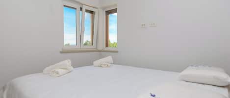 A bedroom with a bed, two pillows, a window, and a wall socket.