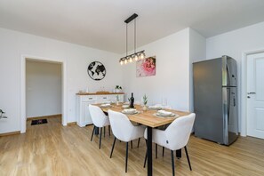 Eine moderne Küche mit Holztisch, weißen Stühlen, einem Edelstahl-Kühlschrank und einer Pendelleuchte.