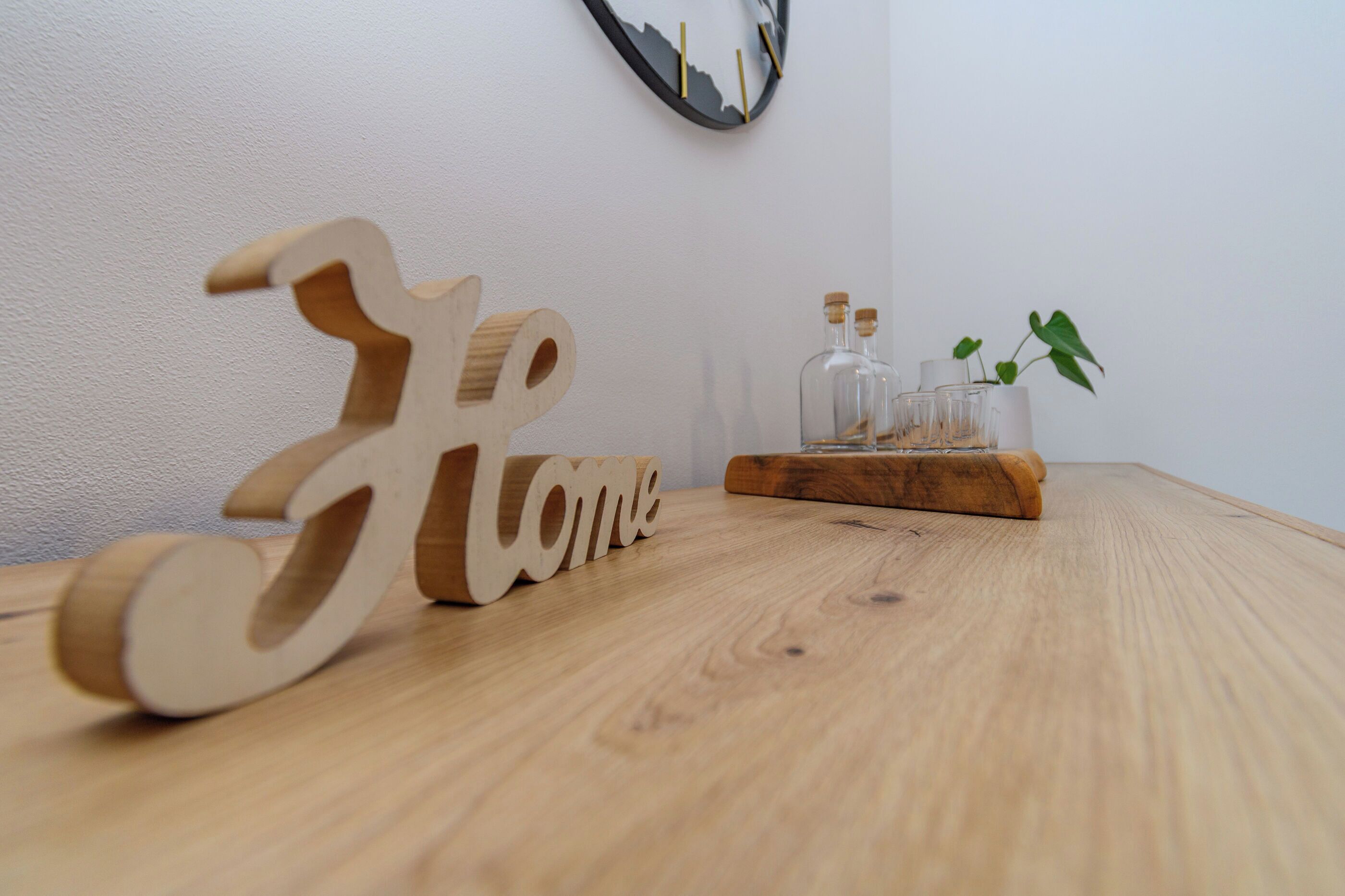 A wooden table with a wooden 'Home' sign, a clock, and a plant with bottles.