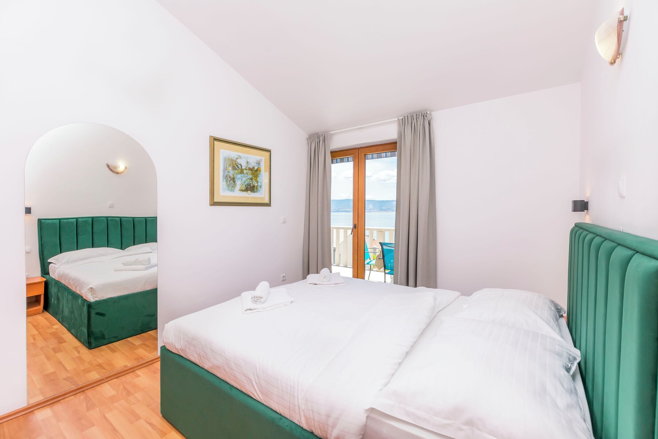 Hotelkamer met een bed, een tafeltje, een stoel, een raam met gordijnen en uitzicht op zee.