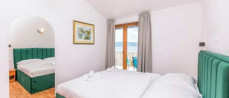 A hotel room with a bed, a small table, a chair, a window with curtains, and a view of the sea.