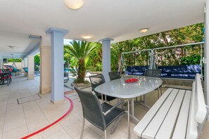 A covered outdoor seating area with a round table and chairs, surrounded by pillars and a view of greenery. - Apartments Wellness&spa (Dugi Rat)