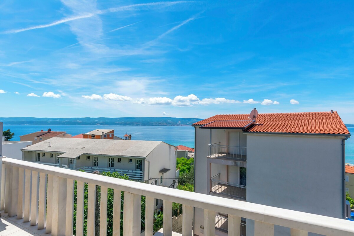A balcony with a railing overlooking a coastal town with buildings and a view of the sea.