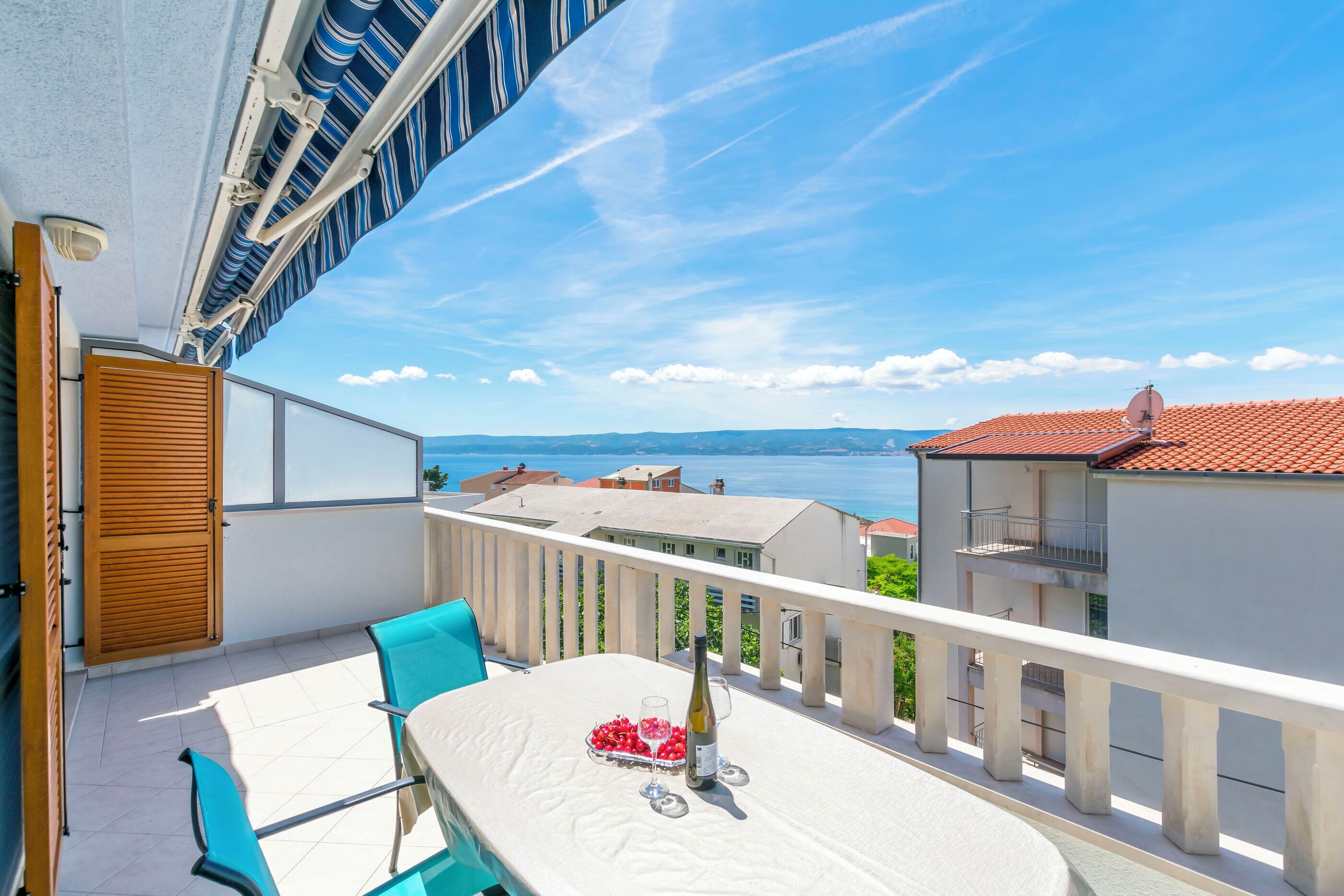 A balcony with a table set for two, a bottle of wine, and a bowl of cherries.