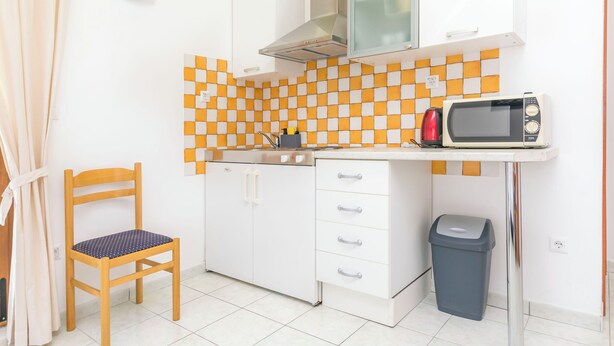 Eine kleine Küchenzeile mit Mikrowelle, Spüle, Schrank, Stuhl und Mülleimer.
