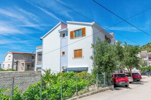 A two-story building with a balcony, a fenced garden, and parked cars. - Apartments Wellness&spa (Dugi Rat)