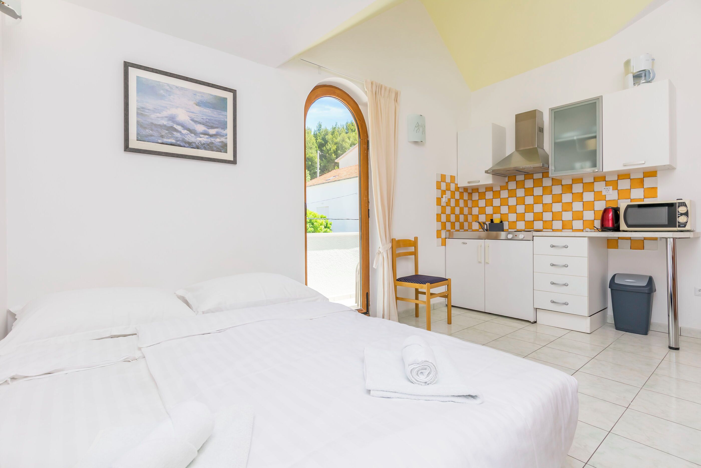 Ein Hotelzimmer mit Bett, Schreibtisch, Stuhl, Mikrowelle, Mülleimer und Blick ins Freie.