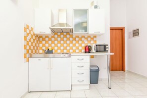 A compact kitchen with white cabinets, a microwave, a kettle, and a tiled backsplash. - Apartments Wellness&spa (Dugi Rat)