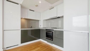 A modern kitchen with white cabinetry, a built-in oven, and a wooden floor. - Canary Wharf Skyline Retreat (London)