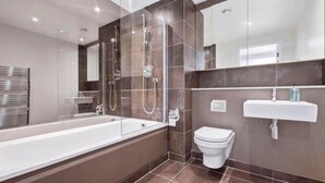 A modern bathroom with a bathtub, toilet, and sink. - Canary Wharf Skyline Retreat (London)