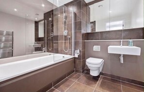 A modern bathroom with a bathtub, toilet, and sink. - Canary Wharf Skyline Retreat (London)
