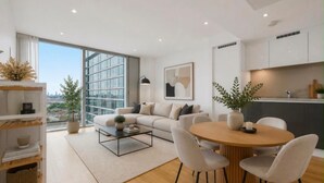 A modern living room with a sofa, coffee table, and dining area. - Canary Wharf Skyline Retreat (London)