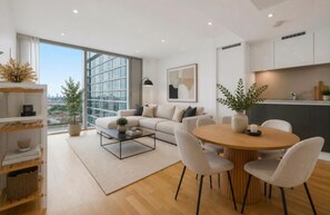A modern living room with a sofa, coffee table, and dining area. - Canary Wharf Skyline Retreat (London)