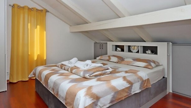 Ein Schlafzimmer mit Bett, einem Fenster mit gelben Vorhängen und einer Decke mit freiliegenden Balken.