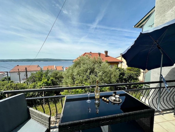 A balcony with a table, a chair, and a view of the sea and buildings. - Apartment Kinaya (Crikvenica)