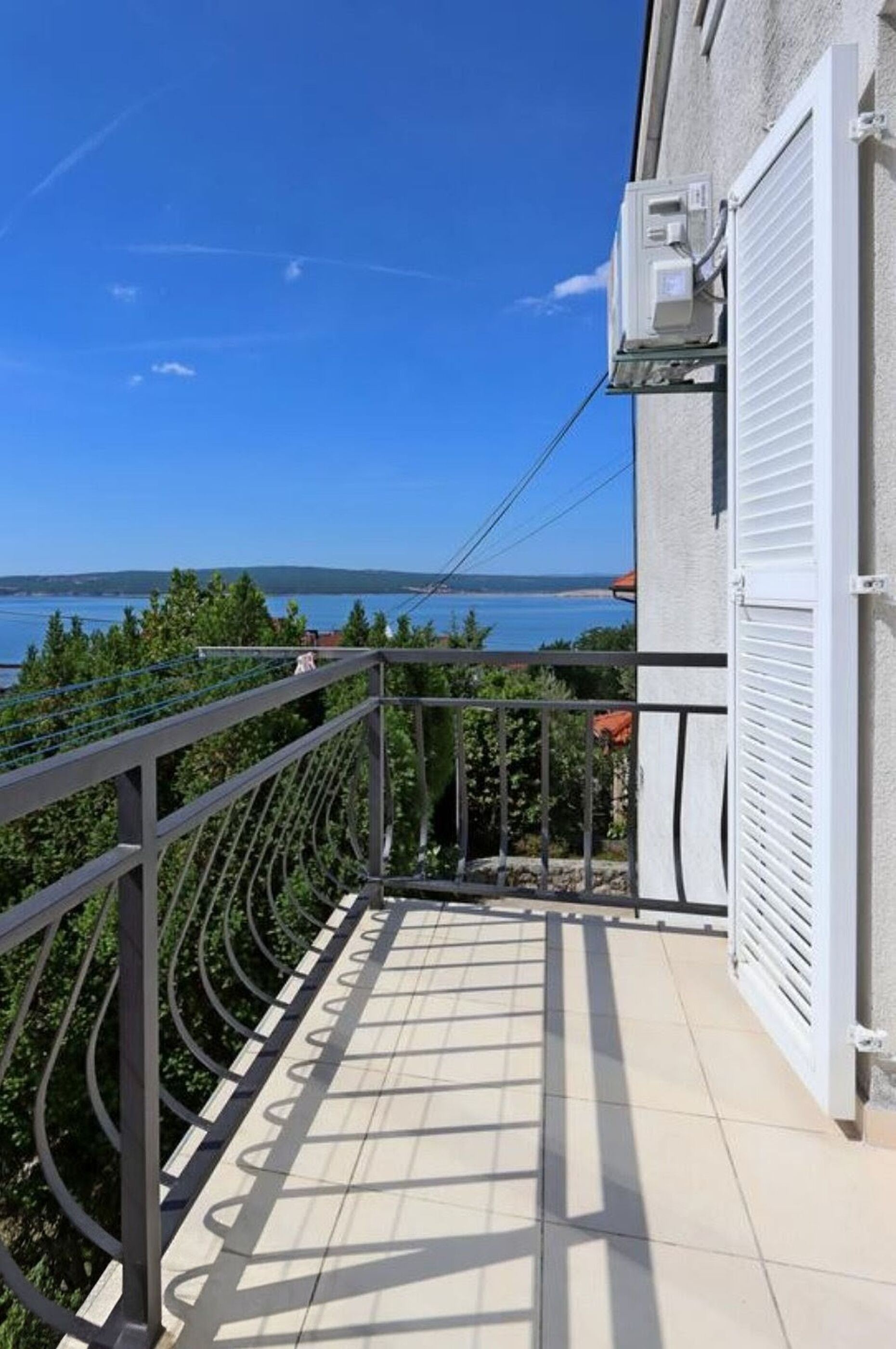 A balcony with a view of the sea, a railing, and a building with a shuttered door.